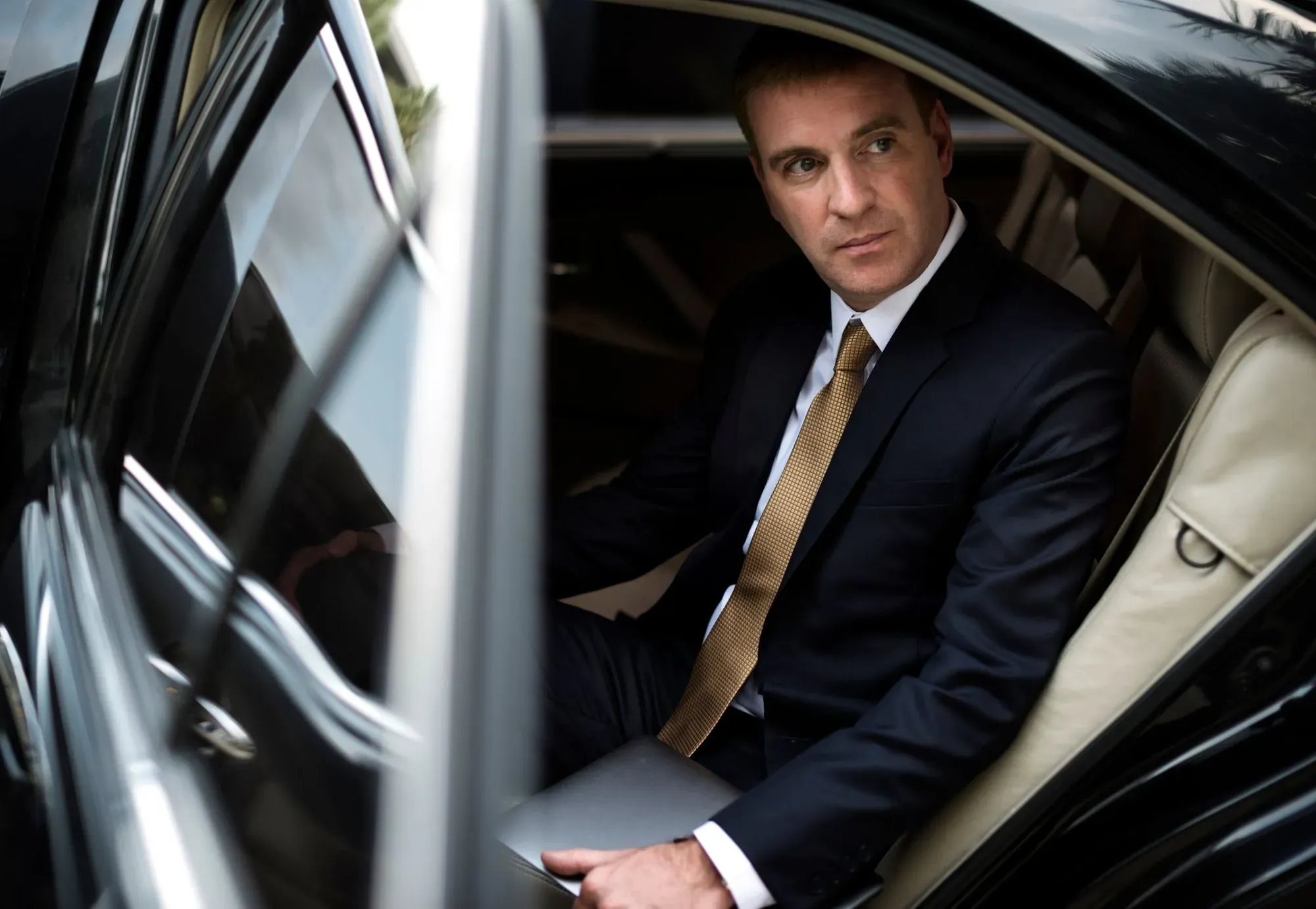 Business traveller in a dark suit in the back of a black car