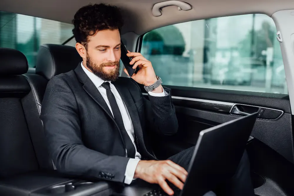 Business traveller on the phone with a laptop in the back seat