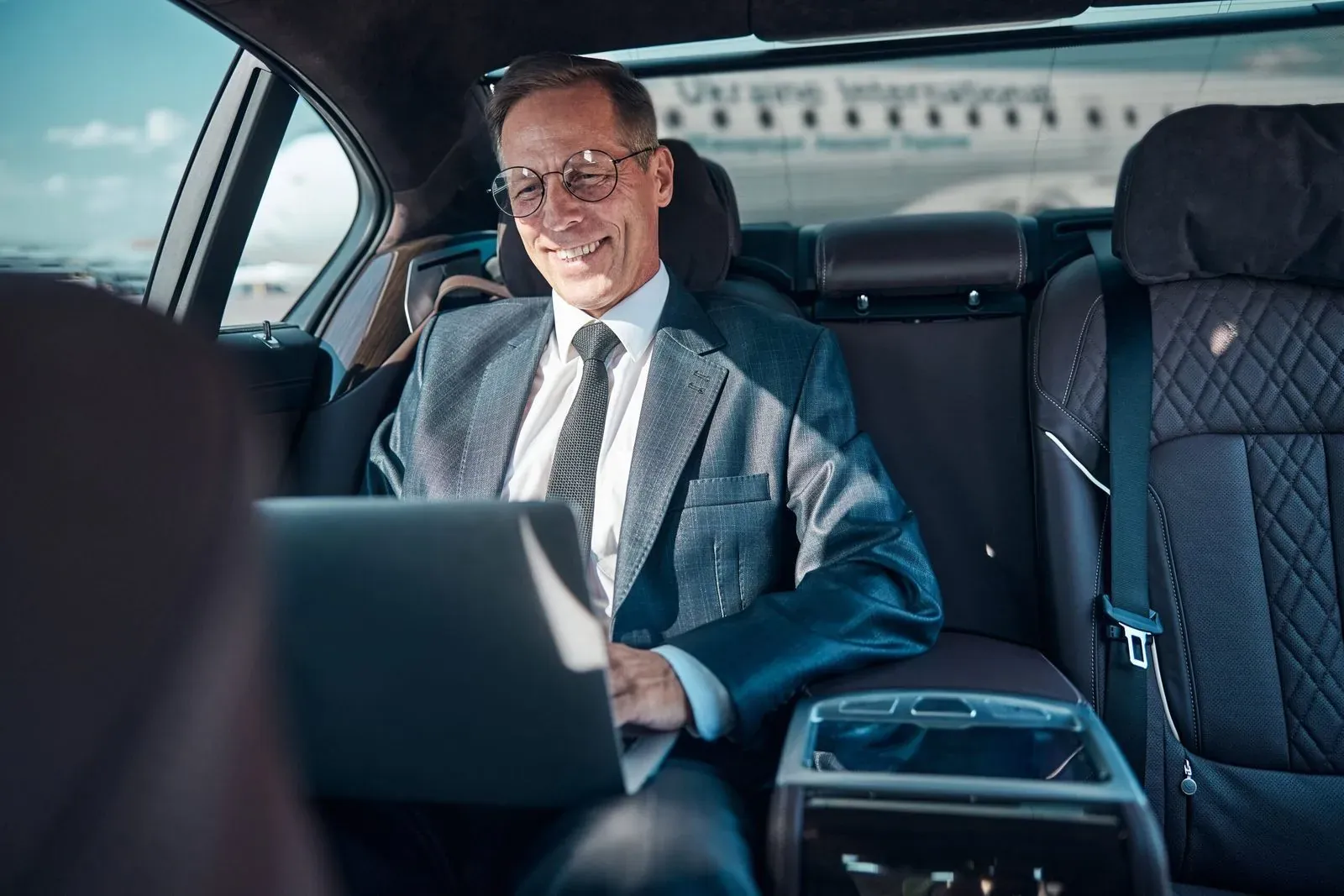 Business traveller with a laptop in the back of a car at the airport