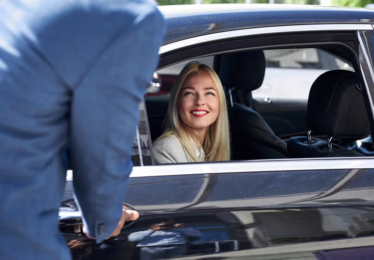 Chauffeur opening the car door for a smiling passenger