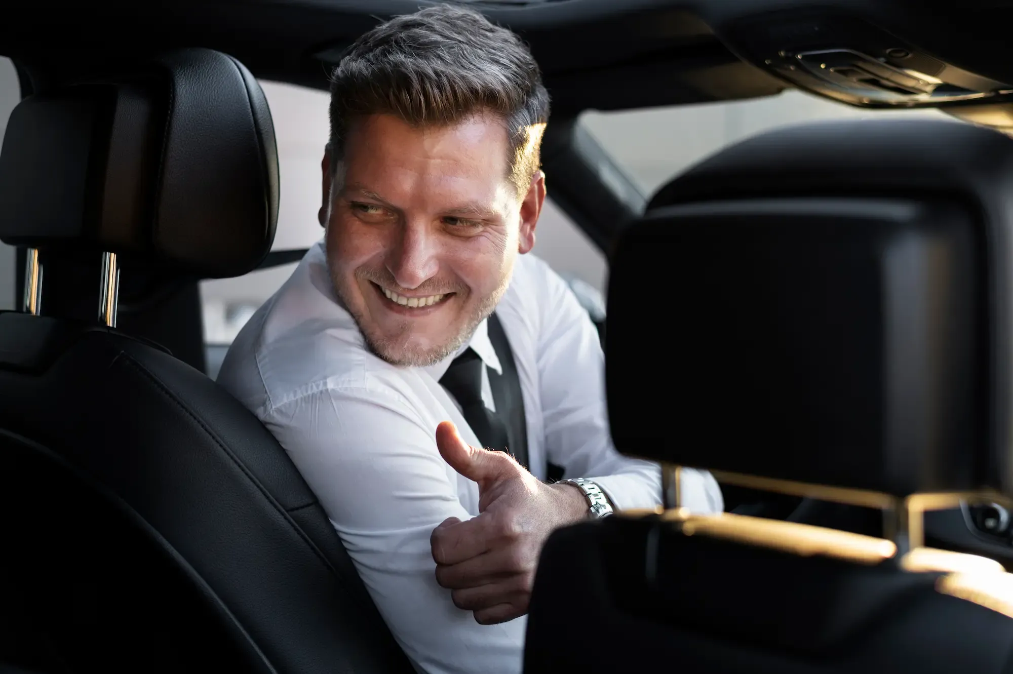 Smiling chauffeur in a white shirt and tie at the wheel